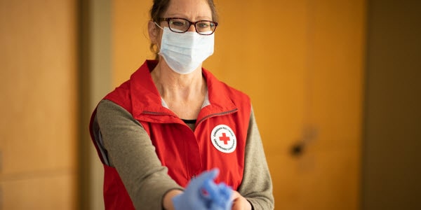 Woman wearing Red Cross vest and medical mask putting on gloves