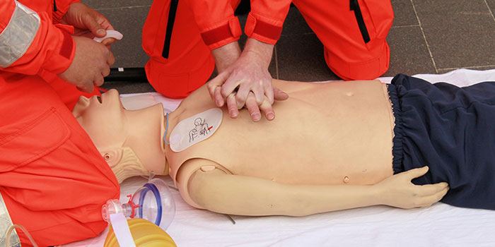 Two people preforming CPR compressions on a dummy.