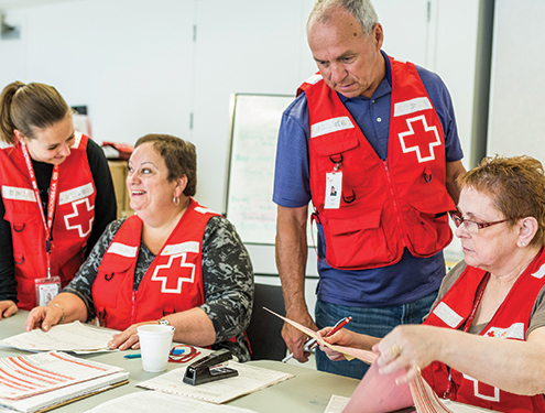 A group of Red Cross volunteers wearing vests, organizing themselves at a table.