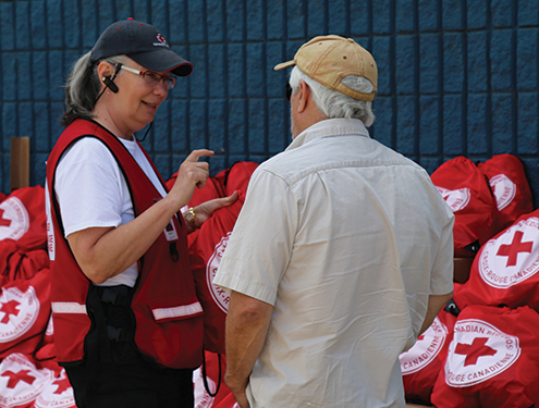 A Red Cross volunteer wearing a headset provides direction to an older man.