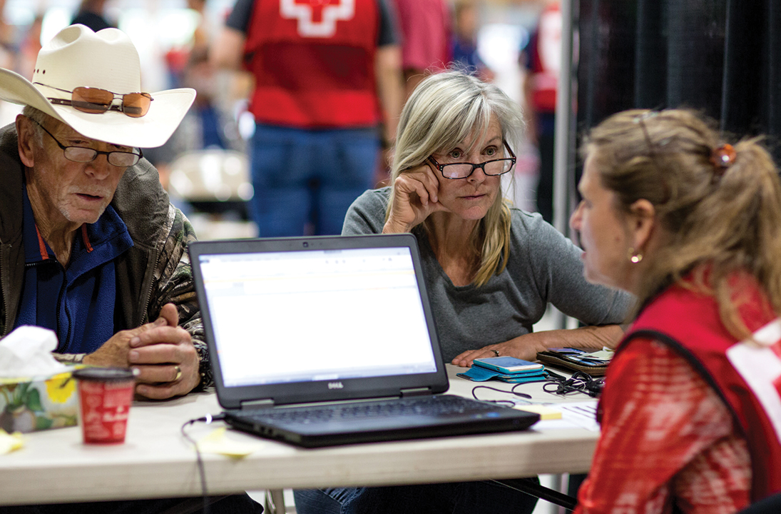 A Red Cross volunteer assists two people in an emergency pop up shelter.