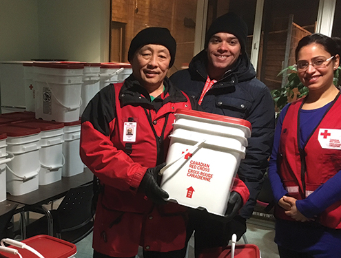 Three Red Cross volunteers smile with large bucket of supplies