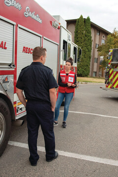 woman in vest with clipboard talks to male firefighter in front of a fire truck