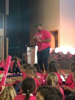 man in pink shirt standing with microphone talking to kids seated on floor