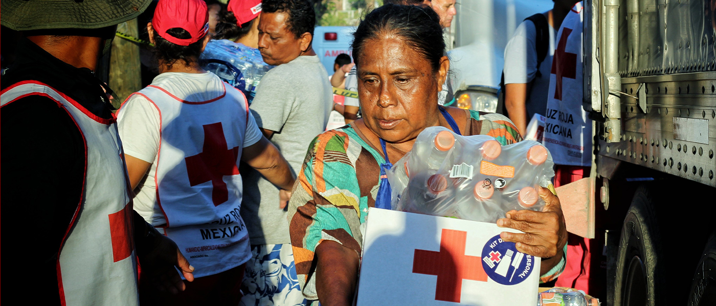 Individual carrying a box with the symbol of the Mexican Red Cross, after hurricane Otis in Mexico.