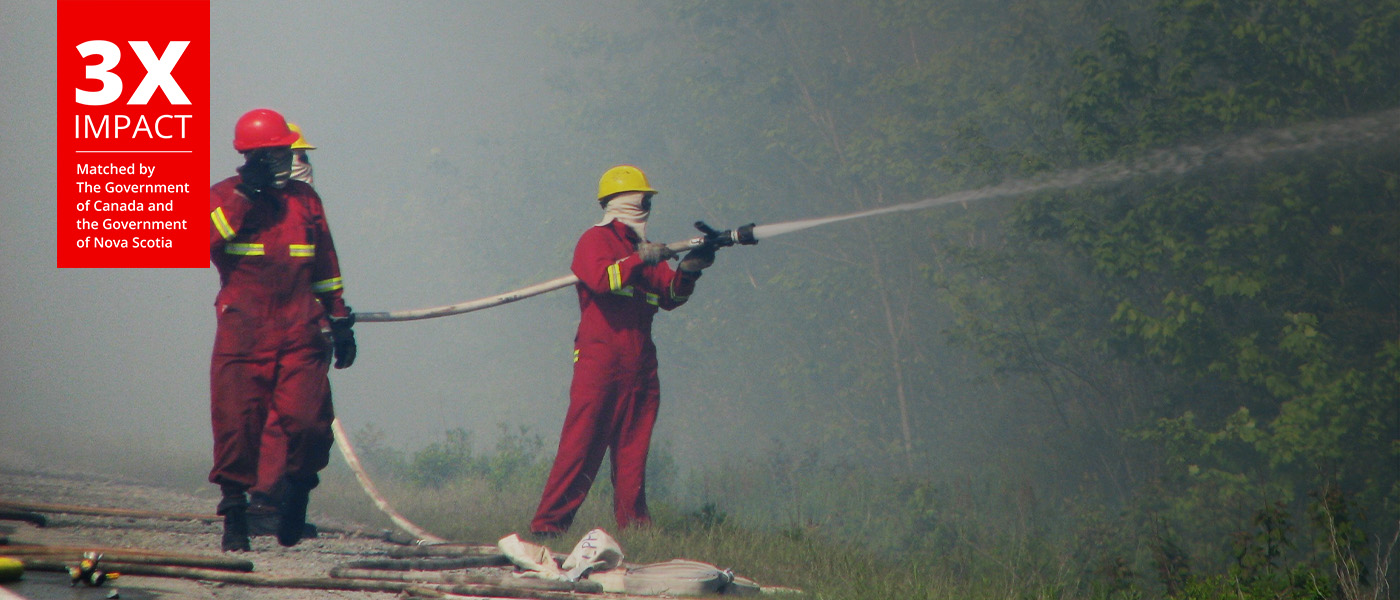 Firemen douse fires with water, with smoke in the background.