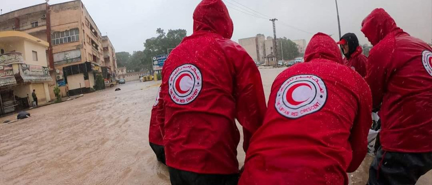 Red Cross Red Crescent volunteers wade through deep flood waters.