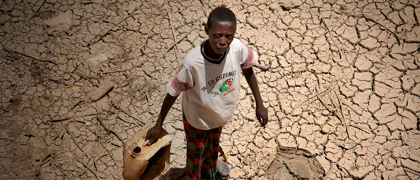 A boy stands with a yellow water jug on arid soil in Somalia.