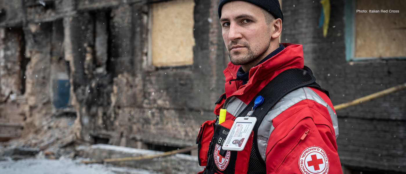 A member of the Ukrainian Red Cross stands in front of a bombed out building.