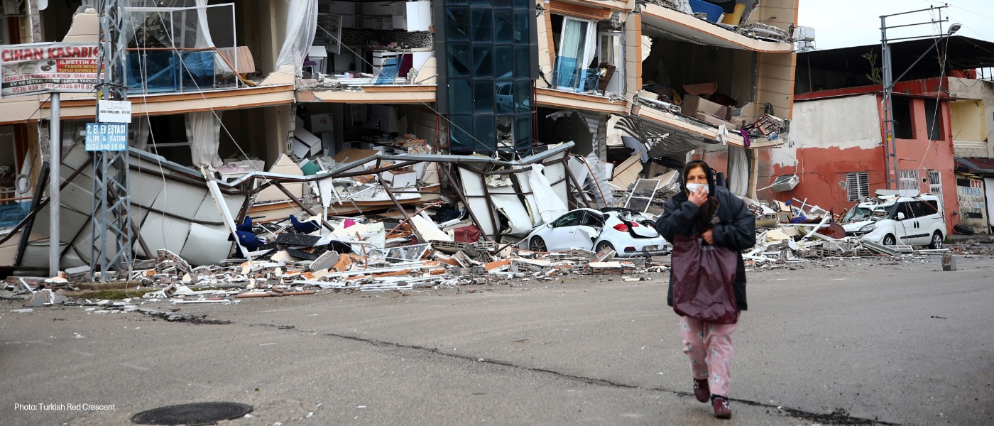 A woman walks in front of a destroyed building in Türkiye after earthquakes hit her country.