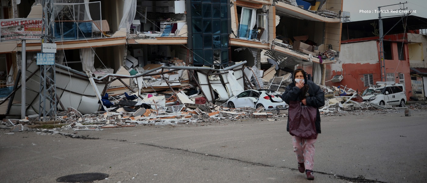 A woman walks in front of a destroyed building in Türkiye after earthquakes hit her country.