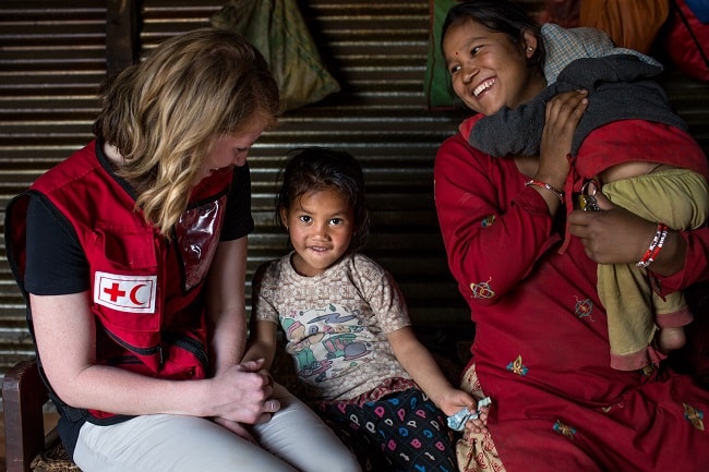 Canadian Red Cross aid worker sitting next to a small child and her mother in Nepal