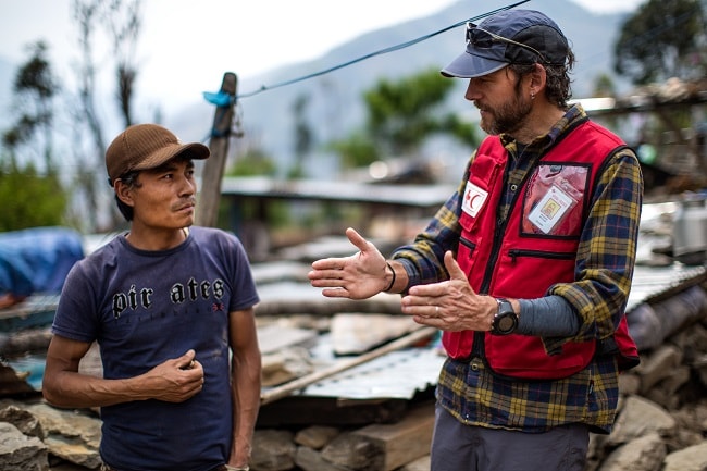 Canadian Red Cross aid worker speaks to local Nepalese man with rubble in background. 