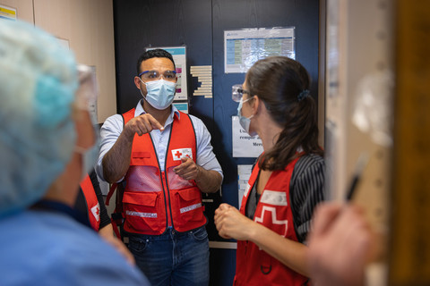 A man wearing a Red Cross vest gives directions to a group of hospital staff and volunteers.