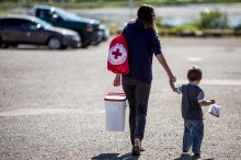 Woman carrying home Red Cross supplies, while walking holding hands with her little boy.