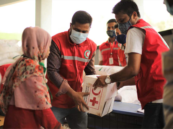 Red Crescent members distribute a box of supplies to a cloaked woman.