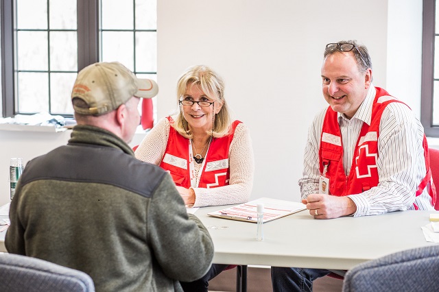 Two Red Cross volunteers talking to an older man at a table