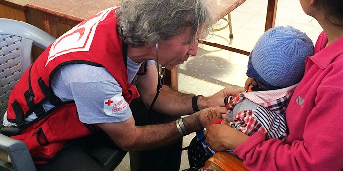 Red Crescent worker taking the pulse of an infant in his mother's arms. 