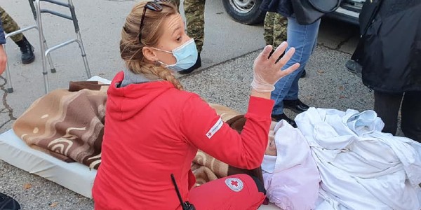 A woman wearing a medical mask is on the ground helping a person, in the street.
