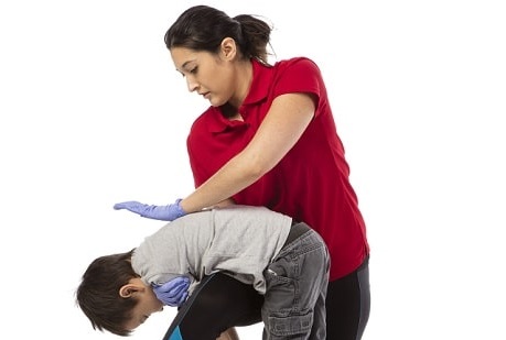 A woman holding a child over her knee while performing back blows to a choking child