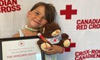 young girl holding teddy bear and certificate smiling at the camera