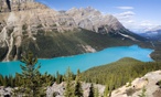 A landscape shot of a turquoise coloured lake, tall trees, and mountains in Alberta.