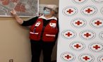 A woman in a Red Cross vest is standing in front of a map