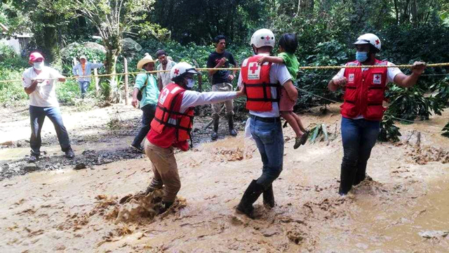 A group of Red Cross workers help a child along a guided rope in a mudslide.