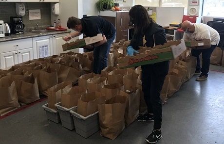 Three people placing items into large paper bags sitting in rows