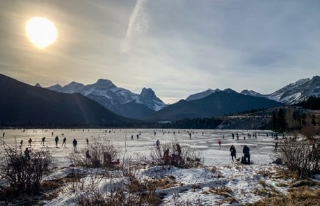 Picture of a lake with people skating and the sun shining in the sky.