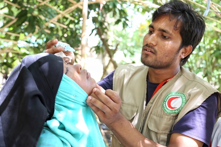 Bangladesh Red Crescent volunteer helps a woman with eye drops