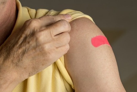 A man uncovers his shoulder with a red bandaid.