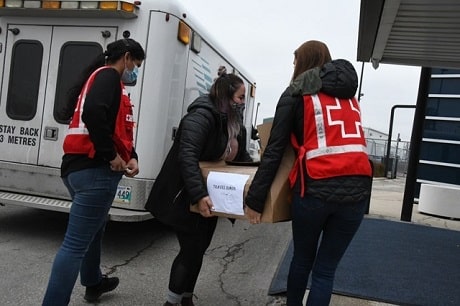 Three people walking by an ambulance, two are carrying a large box
