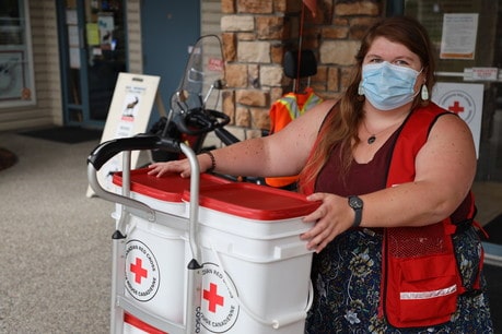A woman in a Red Cross vest wheeling a dolly with clean-up kits on it
