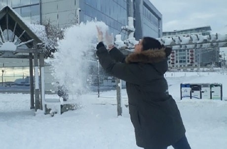 A woman in a winter coat throwing snow into the air