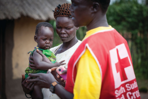 A woman holds a baby as a South Sudan Red Cross personnel walks by.