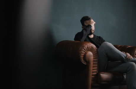A man sitting on a leather couch is holding is head, looking sad