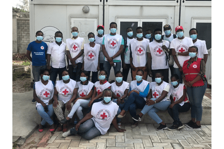 Several people standing or sitting, wearing white Red Cross bibs, posing. 