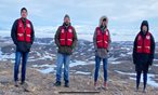 four people in red vests standing outside on the tundra