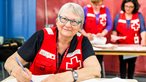 An older female Red Cross volunteer smiles while processing paperwork.