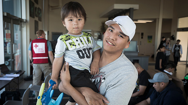 A young man holds a young toddler in his arms, smiling.