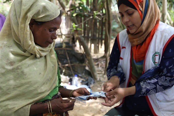 Bangladesh Red Crescent volunteer talks to a woman about medication she is receiving