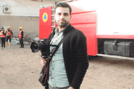 A man stands in front of a trailer with a Canon camera in hand.