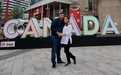 A young man and woman embracing in front of a Canada sign