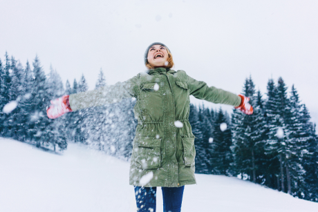 A joyful person stands in the snow, extending their arms, embracing the winter landscape.