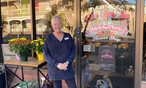 Vicki outside her flower shop with a Pug looking out the door