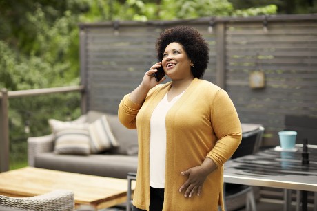A woman wearing a yellow shirt speaks on the phone outside