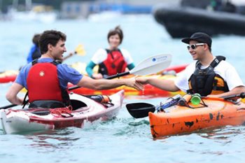 Justin Trudeau wearing a life jacket shakes hands while kayaking with another kayaker