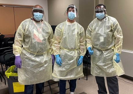 Three people in personal protective equipment including gowns, masks and gloves