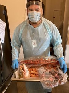 Man in protective mask and scrubs preparing meat in kitchen for Uquutaq Men's Homeless Shelter.